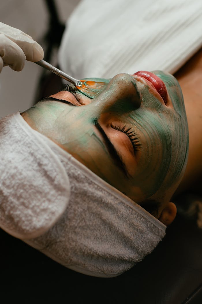 Woman receiving a soothing facial mask treatment at a spa with a brush.